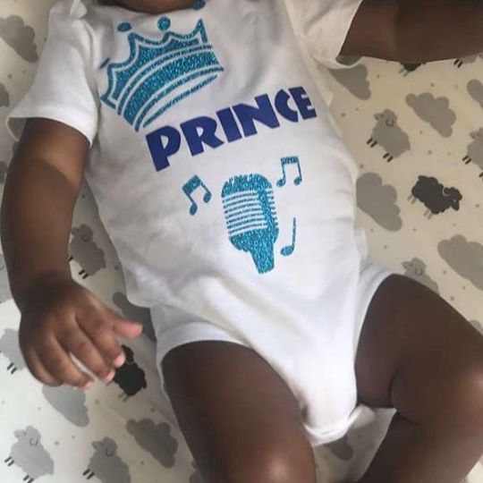 baby wearing customized white onesie that reads "Prince" in blue letters with blue graphics